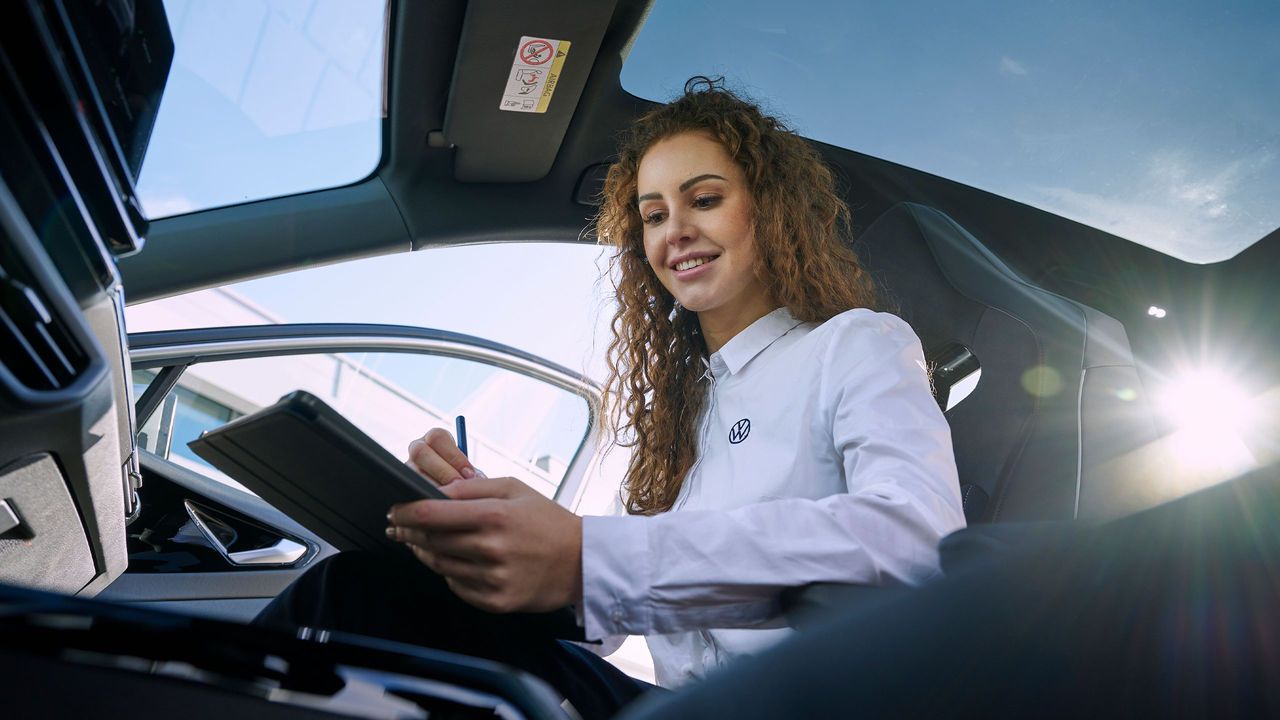 Eine Volkswagen Mitarbeiterin sitzt in eineem Volkswagen und Blickt auf ihr Tablet