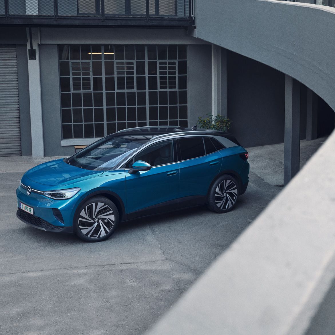 Blauer VW ID.4 parkt in einem Innenhof eines industriellen Gebäudes.