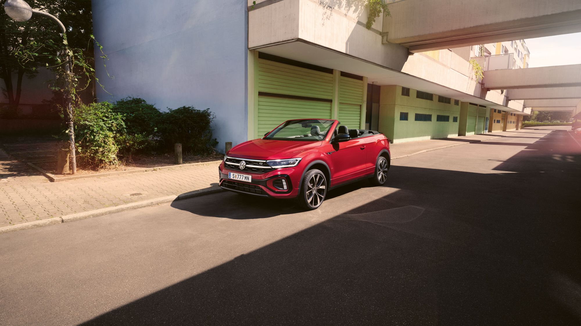 Roter T-Roc Cabriolet steht geparkt am Straßenrand neben dem Gehsteig in einer Stadt.