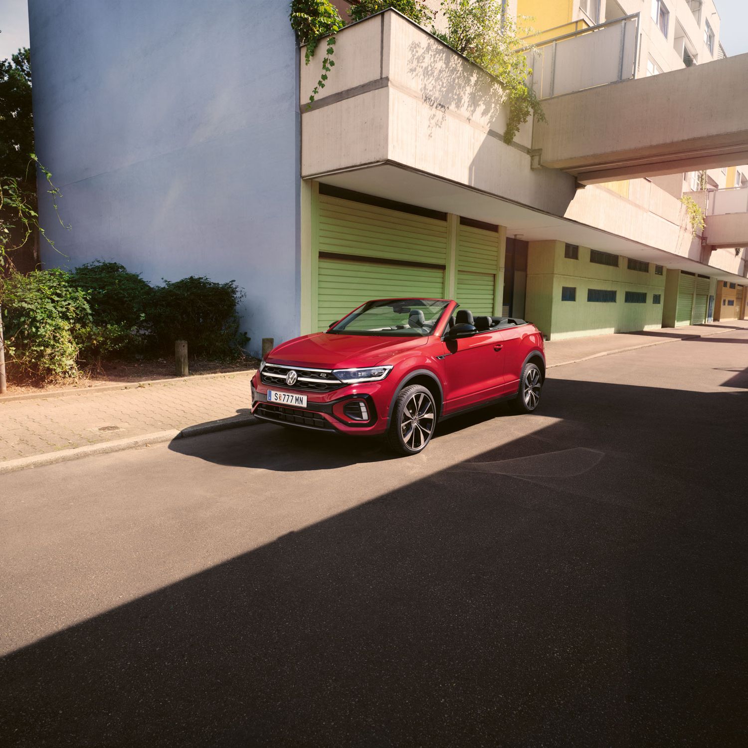 Roter T-Roc Cabriolet steht geparkt am Straßenrand neben dem Gehsteig in einer Stadt.