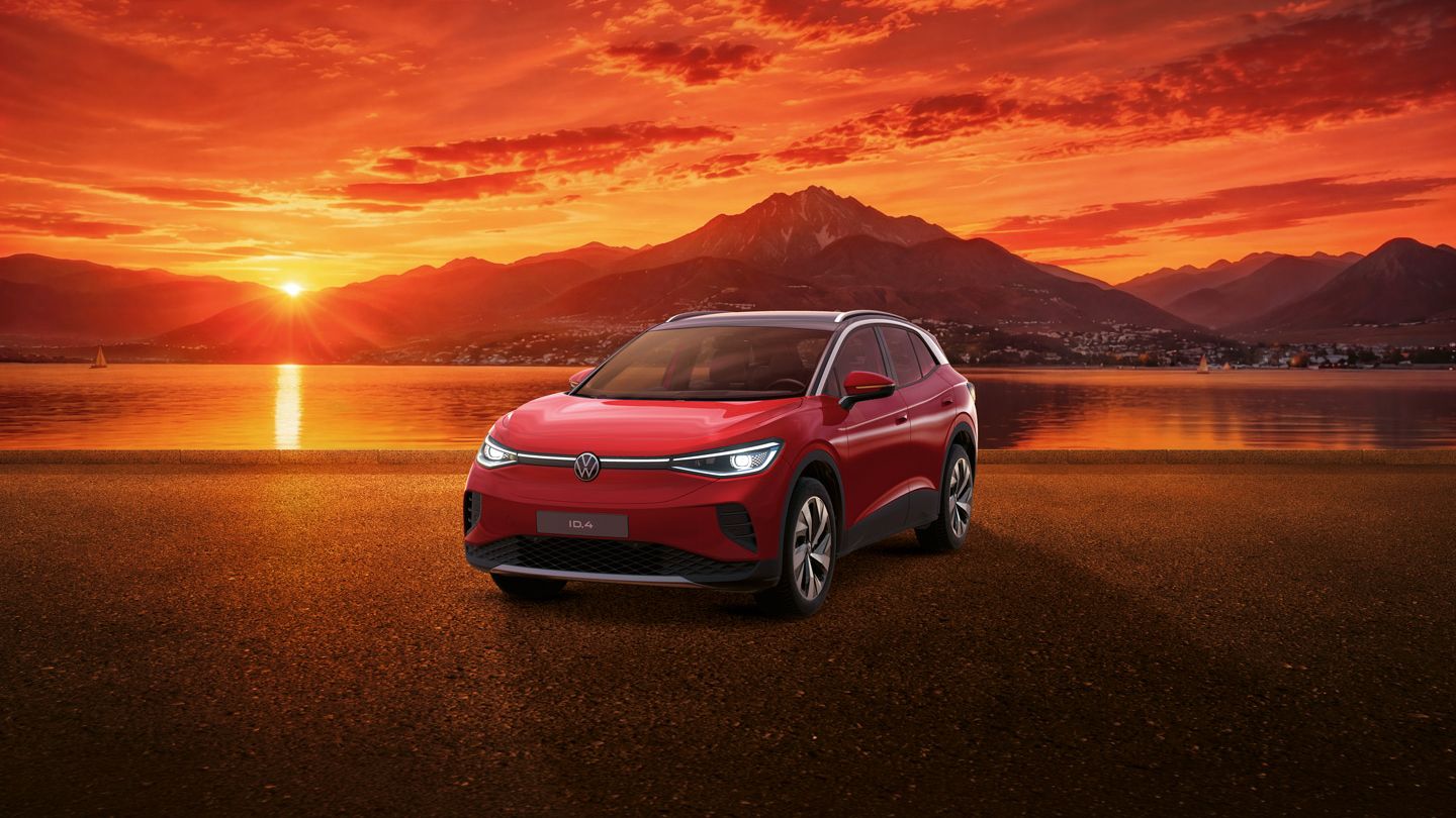 Roter Volkswagen ID.4 steht auf einer ebenen Fläche vor einem See bei Sonnenuntergang. Im Hintergrund spiegeln sich orange‑rote Wolken und die Sonne im Wasser, dahinter erhebt sich eine Bergkette. Die Szene wirkt ruhig und atmosphärisch, mit stark betonten warmen Farben.