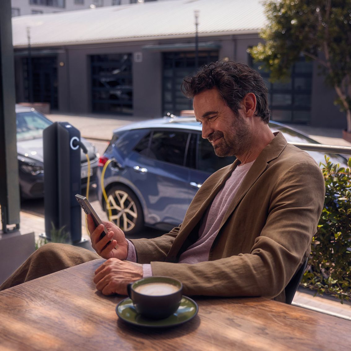 Ein Mann sitzt im Café und checkt per Smartphone den Ladestatus seines VW ID.3 Neo