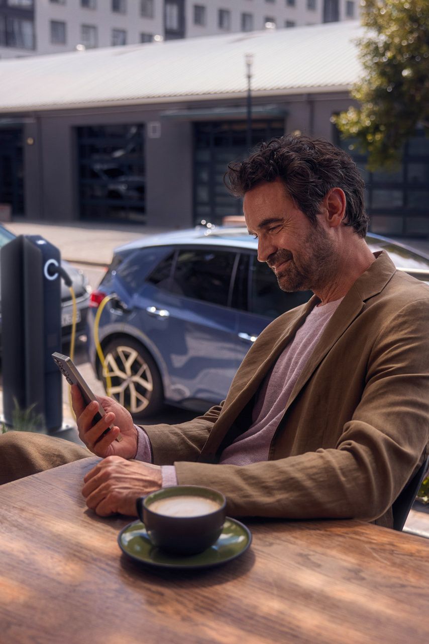 Ein Mann sitzt im Café und checkt per Smartphone den Ladestatus seines VW ID.3 Neo