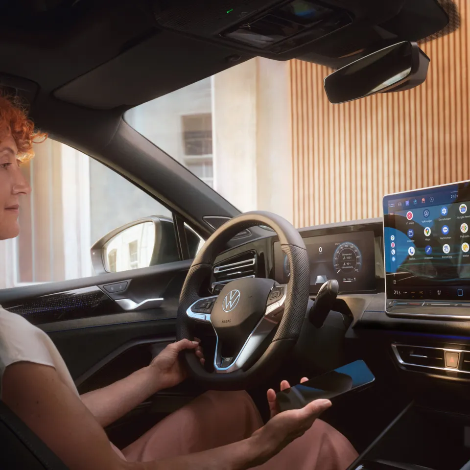 Eine Frau auf dem Fahrersitz des Tiguan hält ein Smartphone in der Hand und blickt auf den Bildschirm des Infotainment-Systems.
