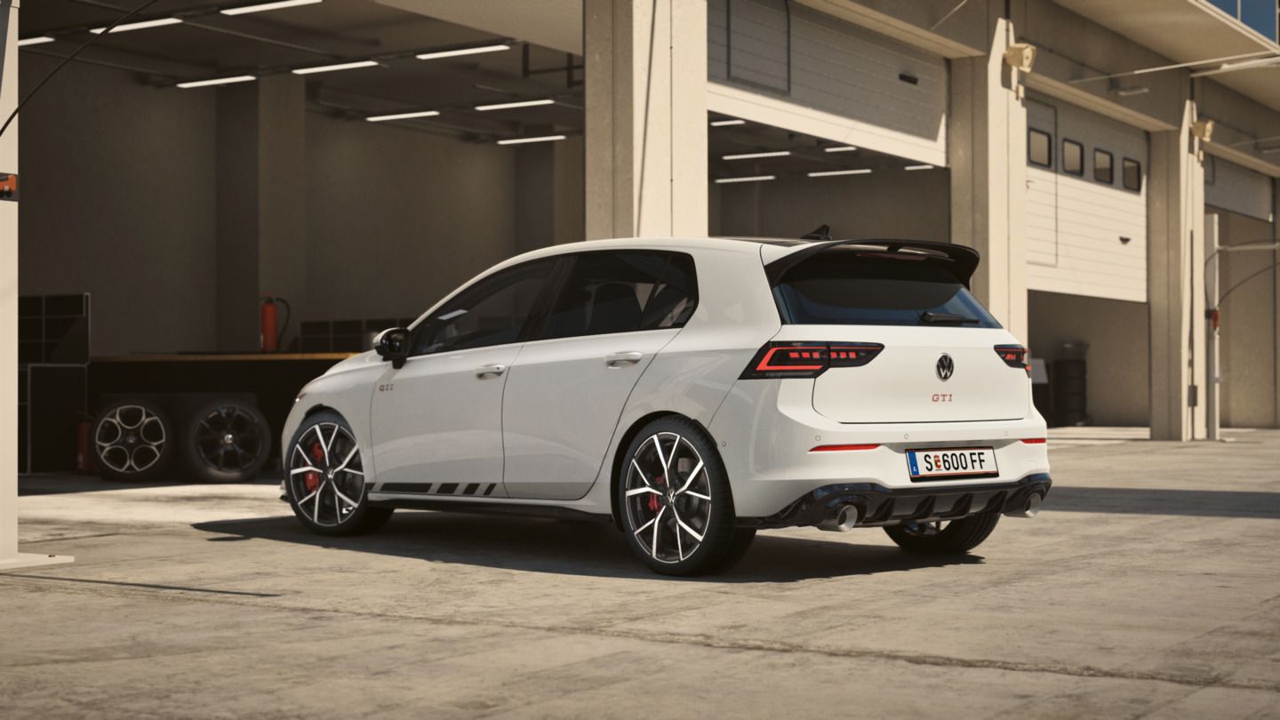 Ein weißer Volkswagen Golf GTI Clubsport steht in einem modernen Garagenkomplex. Das Auto hat schwarze Akzente und rote Bremssättel. Im Hintergrund sind Garage- und Werkstatteinrichtungen sichtbar.