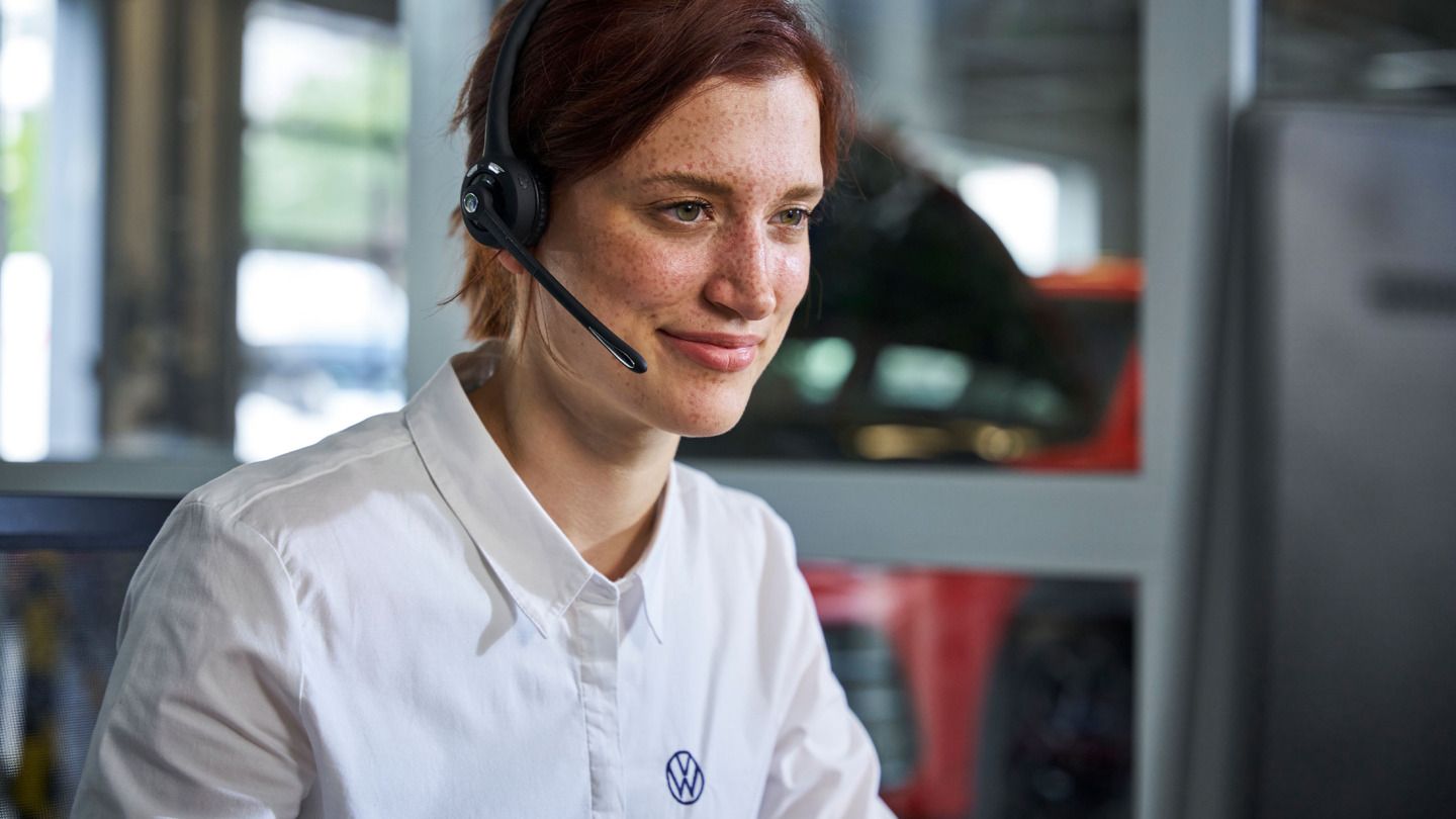 Eine VW Service Mitarbeiterin hat ein Headset auf und ist im Telefonat mit einem Kunden.