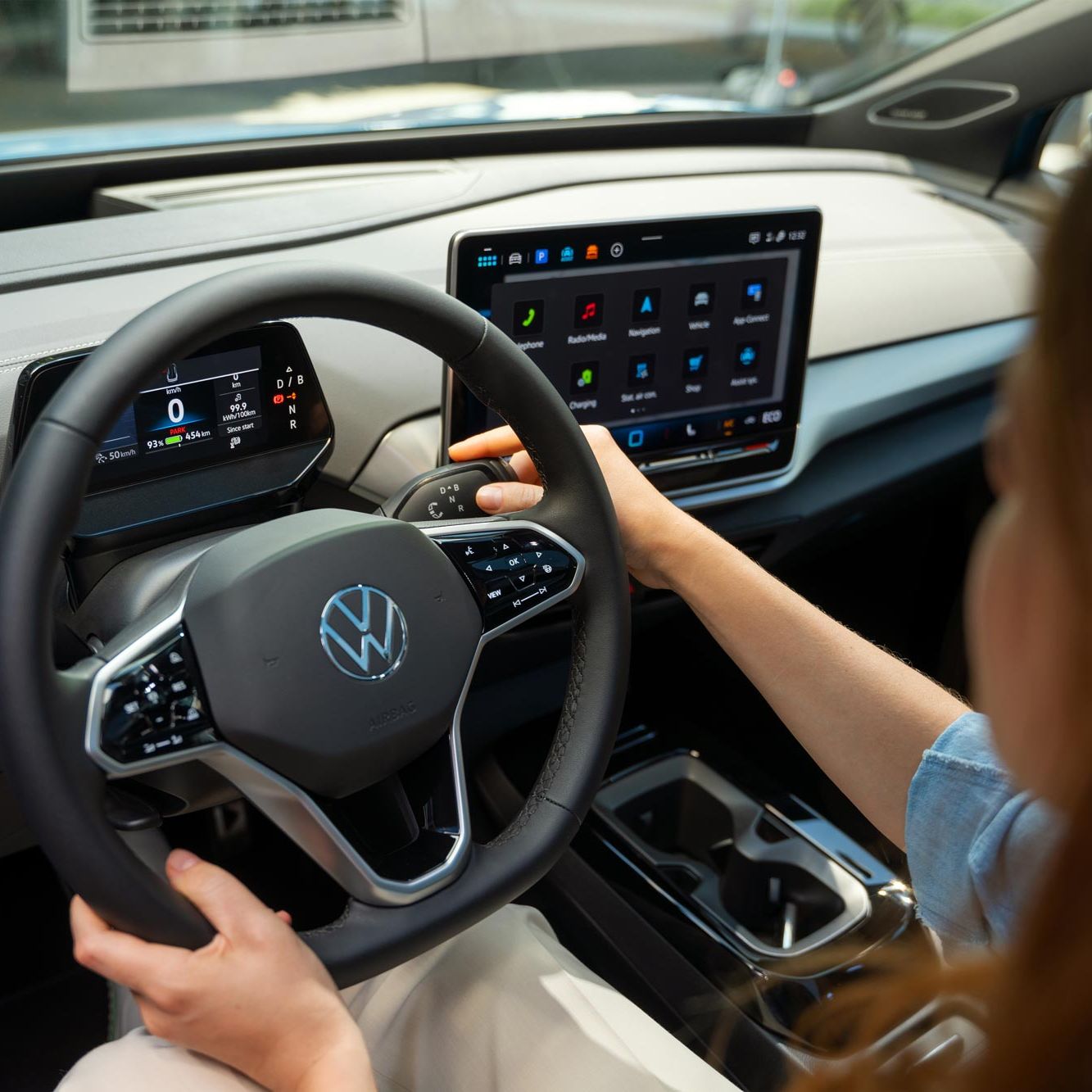 Innenansicht eines stehenden VW ID.4. Eine Frau sitzt auf dem Fahrersitz, ihre rechte Hand bedient den Schalthebel am Lenkrad.