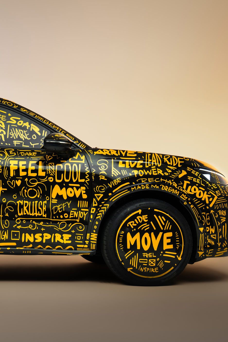 Der neue T-Roc, der vollständig mit gelben handgeschriebenen Worten und Illustrationen bedeckt ist. Die Wörter umfassen positive und inspirierende Begriffe wie "Flow", "Move" und "Inspire". Das Fahrzeug steht vor einem hellbraunen Hintergrund.