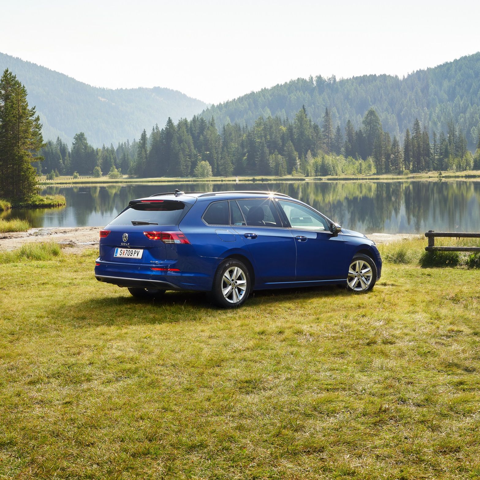 Ein blauer VW Golf Variant steht auf einer Wiese vor einem See