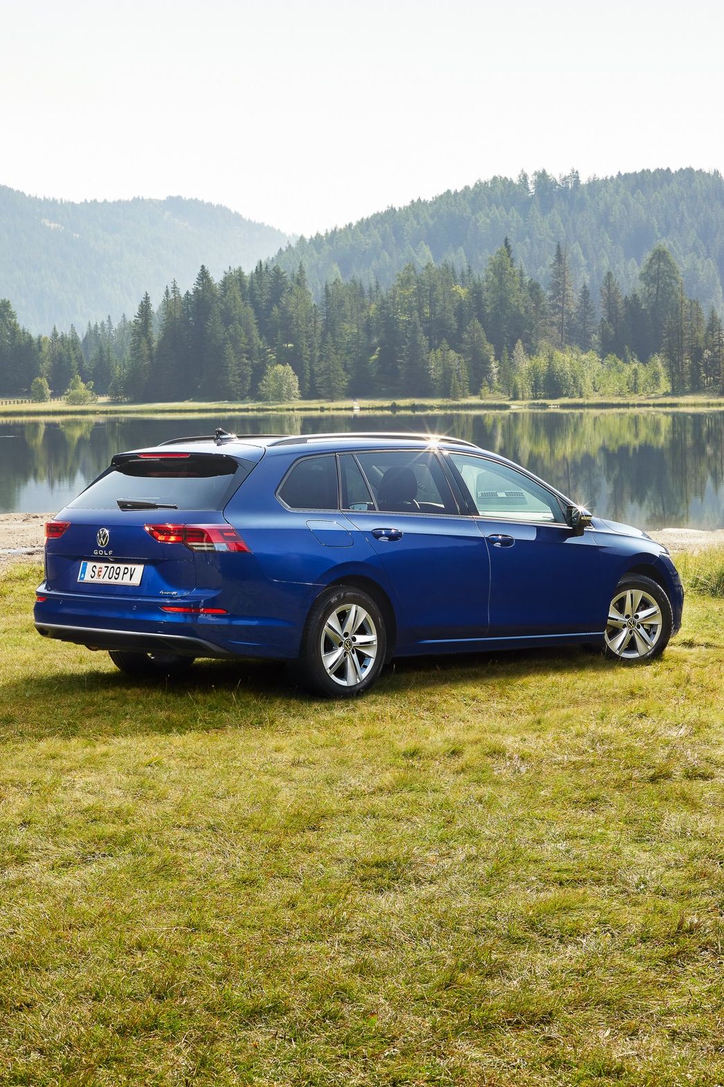 Ein blauer VW Golf Variant steht auf einer Wiese vor einem See