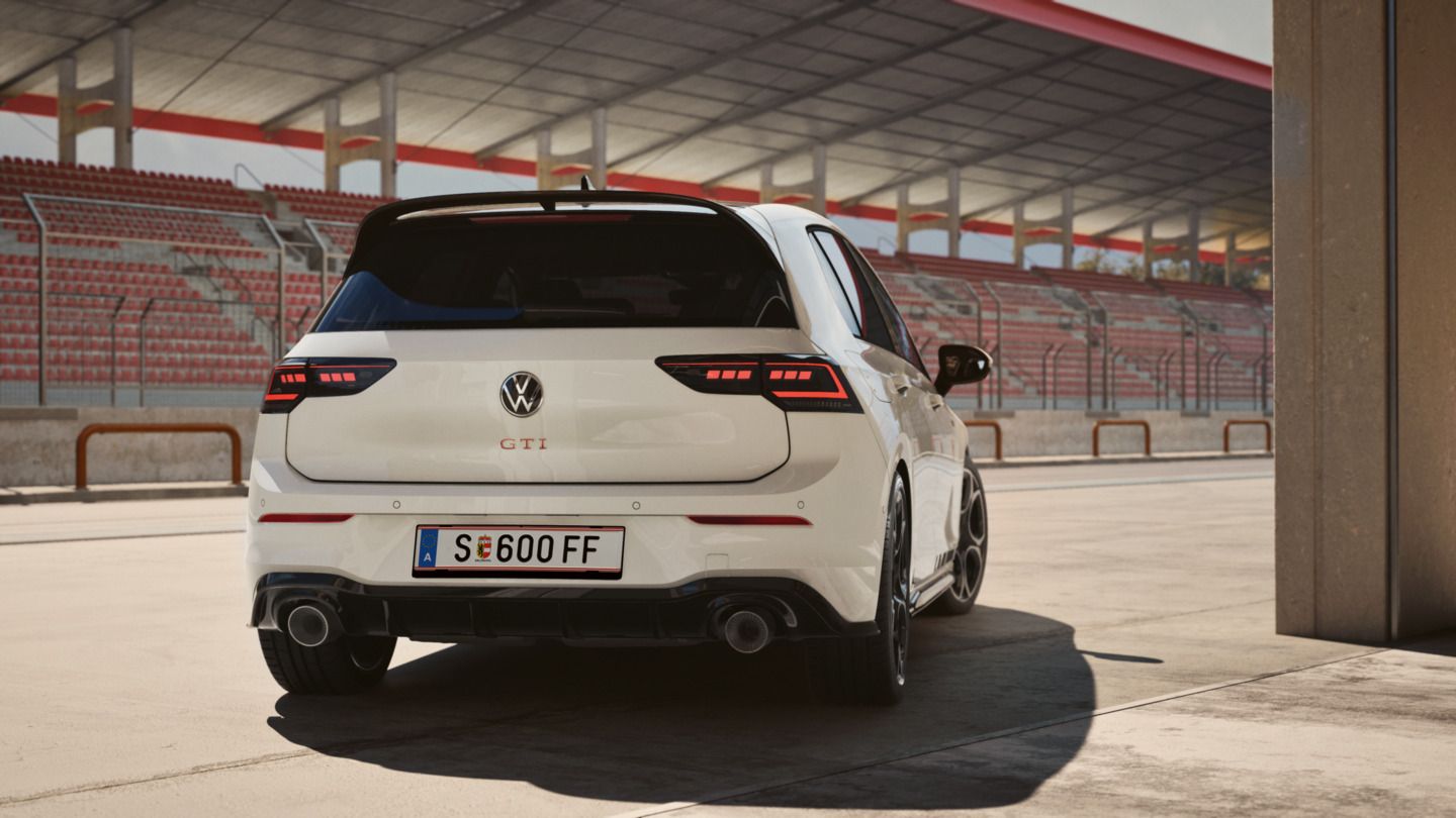 Ein weißer Volkswagen Golf GTI Clubsport steht vor einer Rennstrecken-Tribüne. Das Auto hat sportliche Rückleuchten und einen Doppelrohrauspuff. Das Nummernschild zeigt "S E 600 FF".