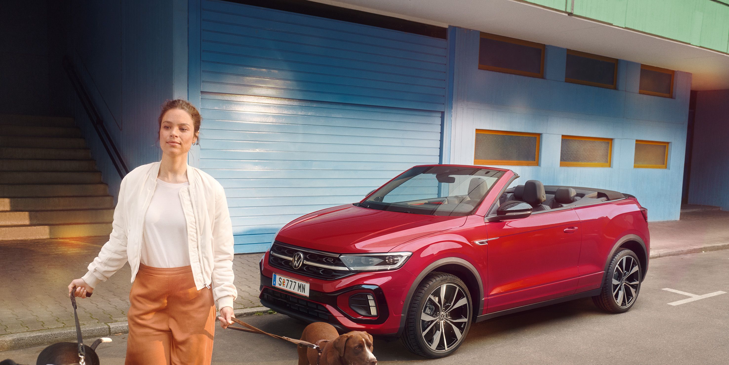 Frau geht mit zwei Hunden and der Leinen von einem roten VW T-Roc Cabrio weg