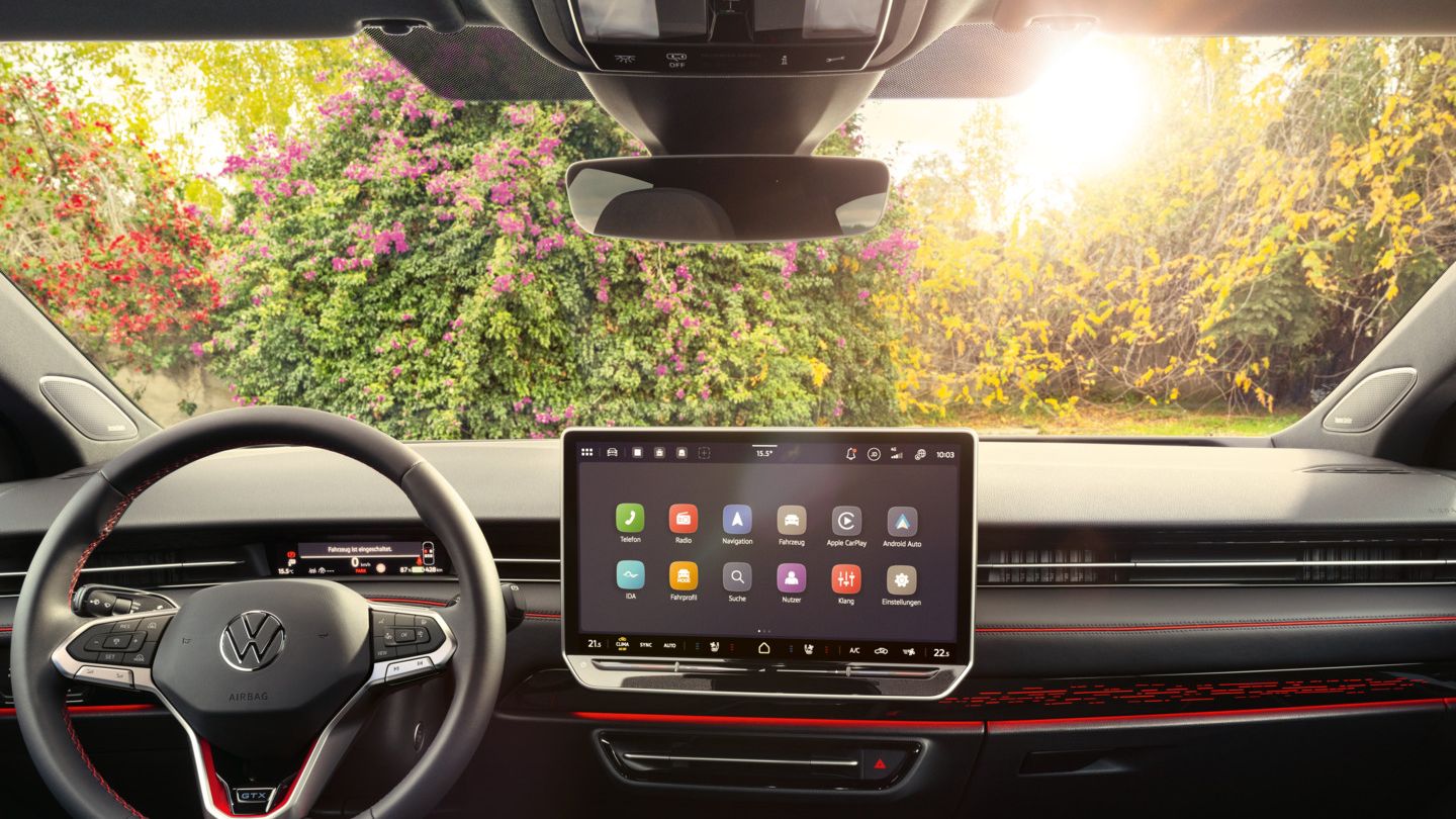 Interieur des ID.7 GTX mit roter Ambientebeleuchtung, roten Ziernähten am Multifunktionslenkrad und dem Infotainmentsystem. 