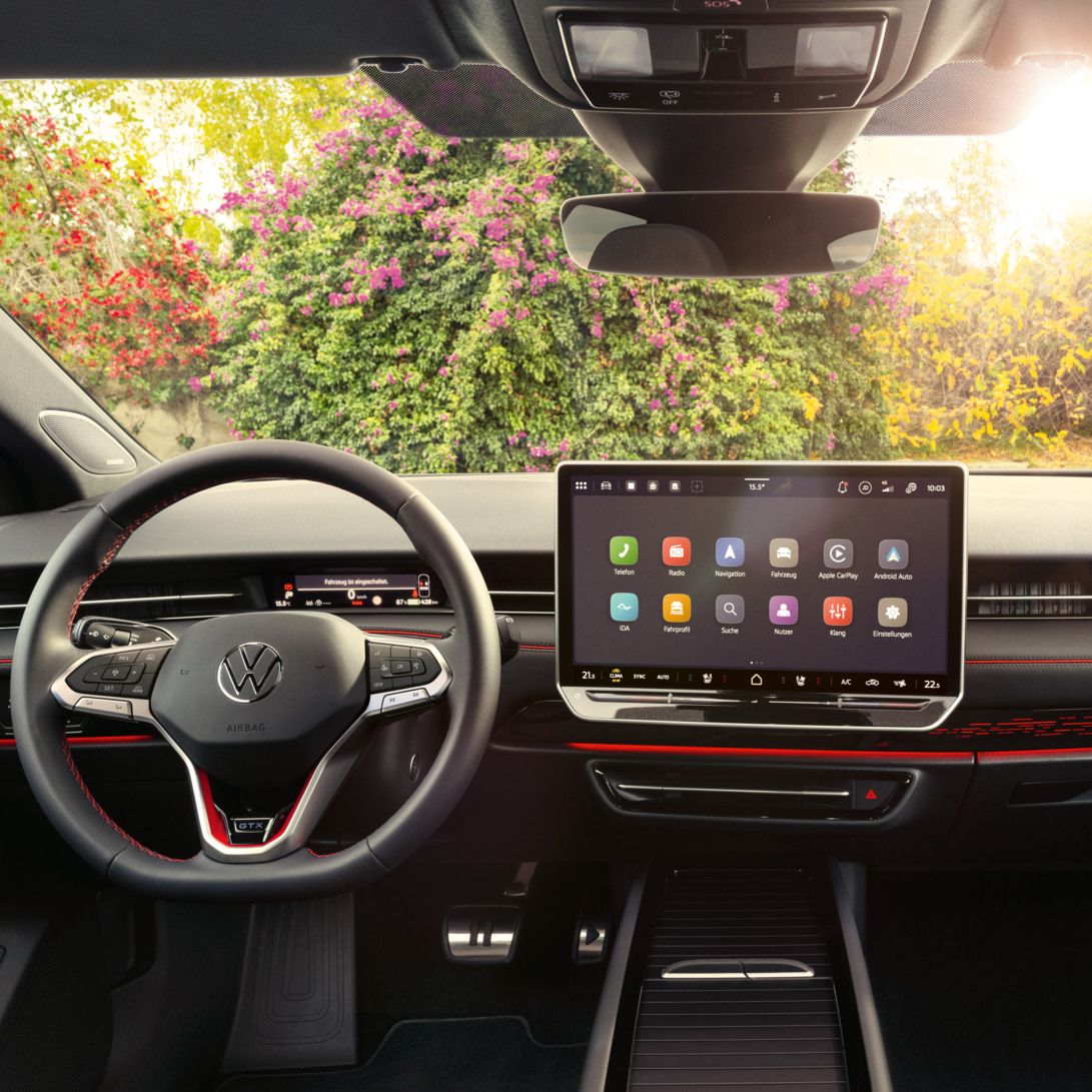 Interieur des ID.7 GTX mit roter Ambientebeleuchtung, roten Ziernähten am Multifunktionslenkrad und dem Infotainmentsystem. 