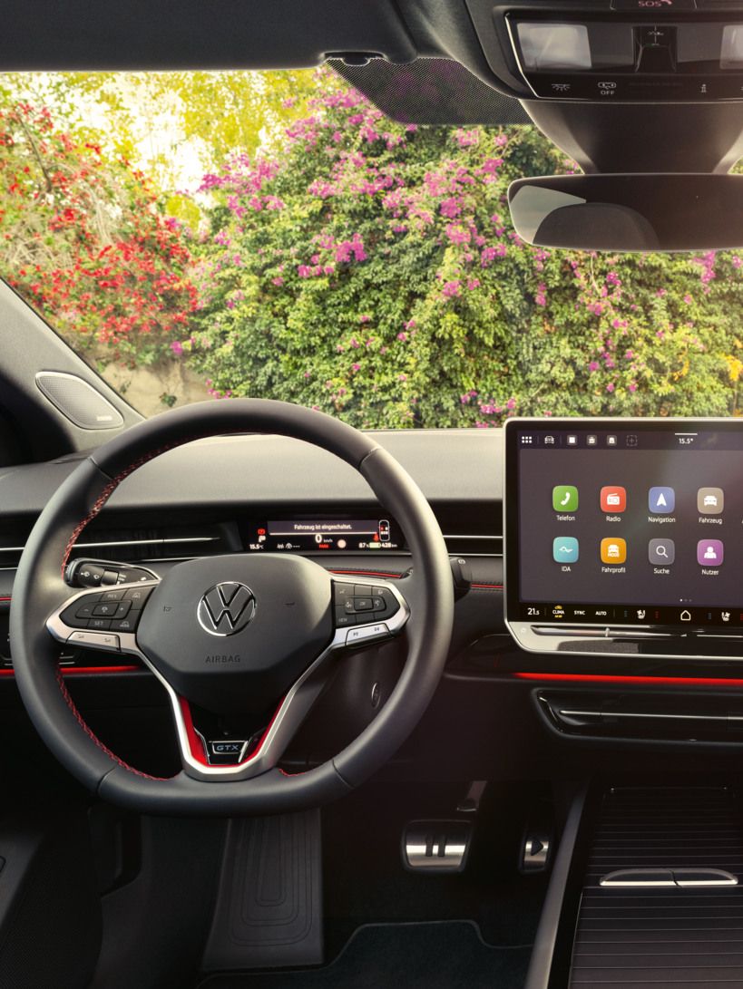 Interieur des ID.7 GTX mit roter Ambientebeleuchtung, roten Ziernähten am Multifunktionslenkrad und dem Infotainmentsystem. 