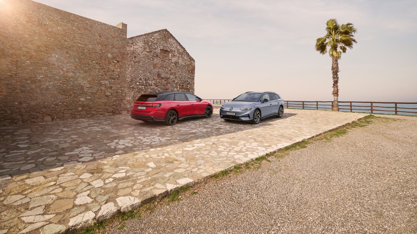 Ein roter VW ID.7 GTX Tourer und ein blauer VW ID.7 Tourer stehen auf einer Parkfläche am Meer.