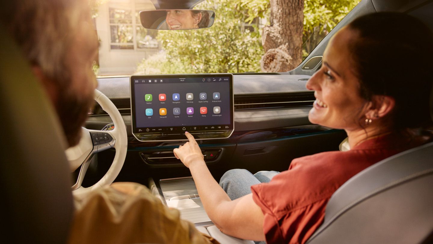 Zwei Personen sitzen auf den Vordersitzen des VW ID.7 und schauen sich lachend an. In der Mitte ist das Infotainment des VW ID.7 zu sehen. 