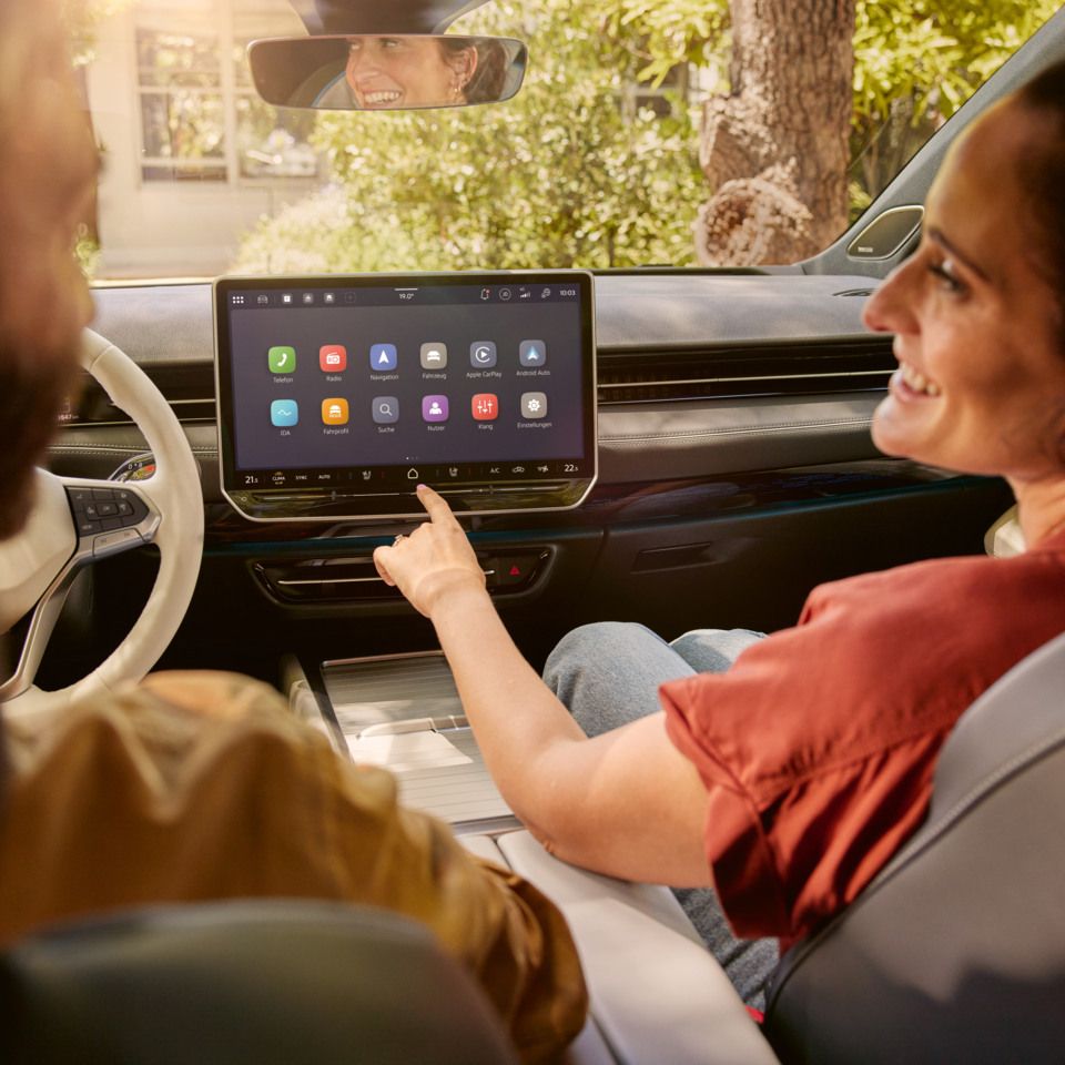 Zwei Personen sitzen auf den Vordersitzen des VW ID.7 und schauen sich lachend an. In der Mitte ist das Infotainment des VW ID.7 zu sehen. 