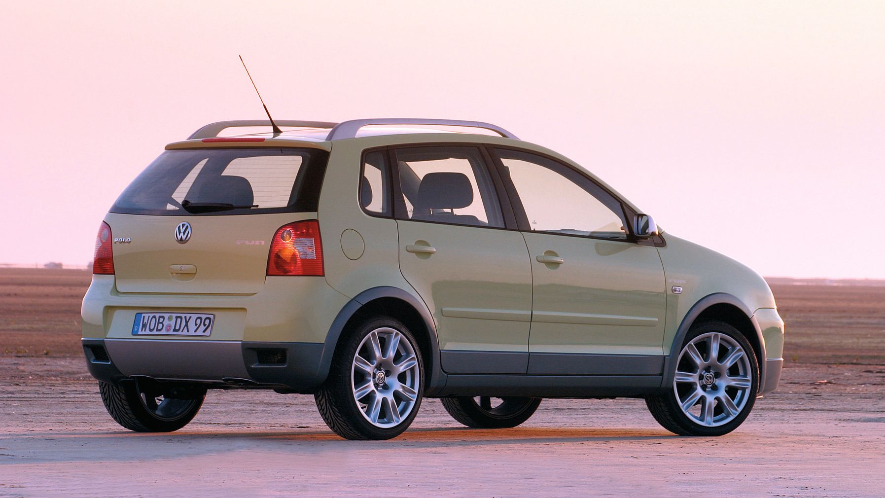 Ein grüner VW Polo FUN steht auf einer ebenen Fläche bei Sonnenuntergang. Die Kamera zeigt die Rückseite und linke Seite des Autos. Das Kennzeichen lautet WOB-DIX 99.