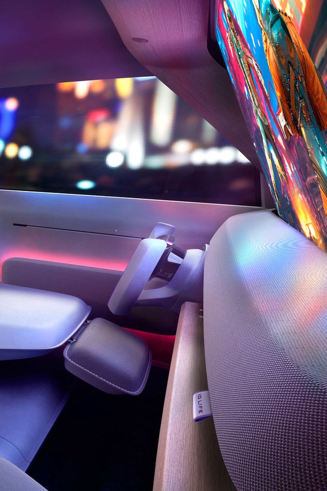 Innenraum eines ID. LIFE mit einem zurückgeklappten Sitz, der wie ein Bett aussieht. Das Armaturenbrett hat ein großes digitales Display. Durch die Fenster sind unscharfe Lichter einer Stadt bei Nacht zu erkennen.