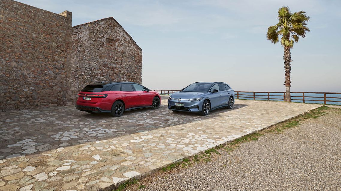 Ein roter VW ID.7 GTX Tourer und ein blauer VW ID.7 Tourer stehen auf einer Parkfläche am Meer.