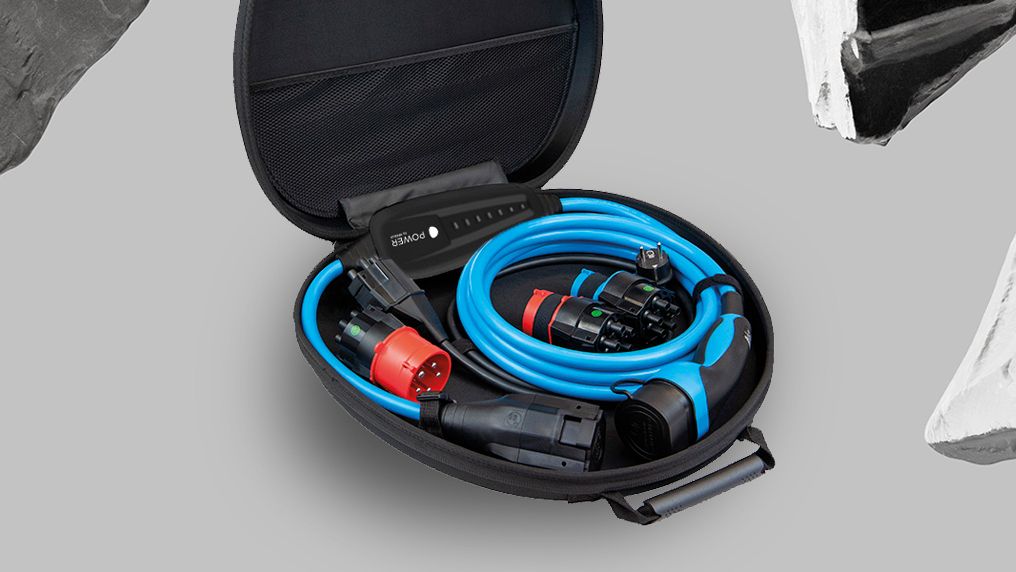 Ein offener, ovaler Koffer enthält blaue und schwarze Kabel sowie Anschlüsse. Der Hintergrund ist grau und mit schwarz-weißen Gesteinsformen verziert. Das Bild zeigt Ausrüstung für den Anschluß von Elektrofahrzeugen.