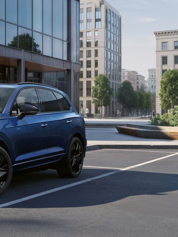 Ein blauer VW Touareg Final Edition steht vor einem Bürogebäude mit Glasfassade - Ansicht von schräg vorne.