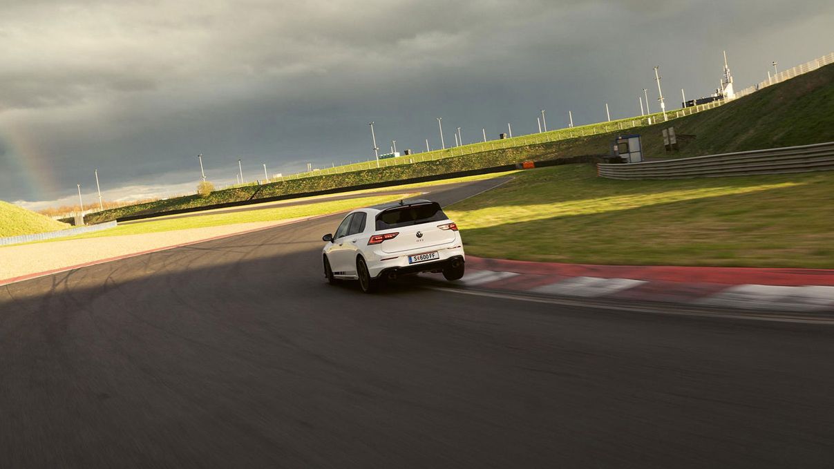 Heckansicht eines weißen VW Golf GTI Clubsport, der auf einer Rennstrecke in eine Kurve fährt.
