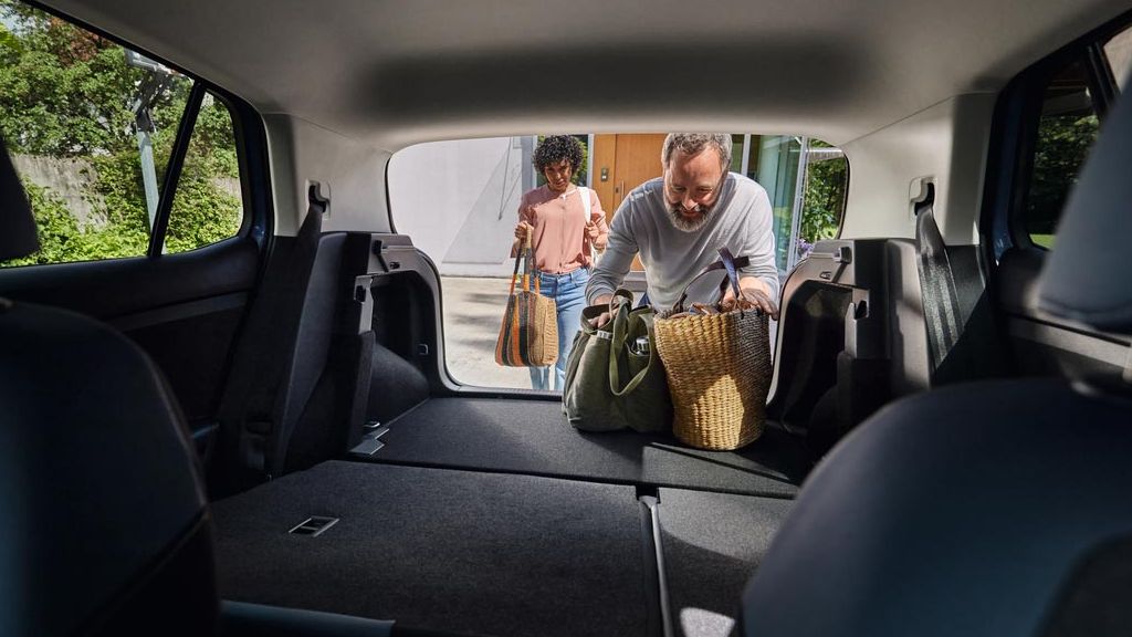 Blick von den Vordersitzen auf die umgeklappten Rücksitze und Kofferaum eines VW T-Cross. Ein Mann lädt Taschen ein.