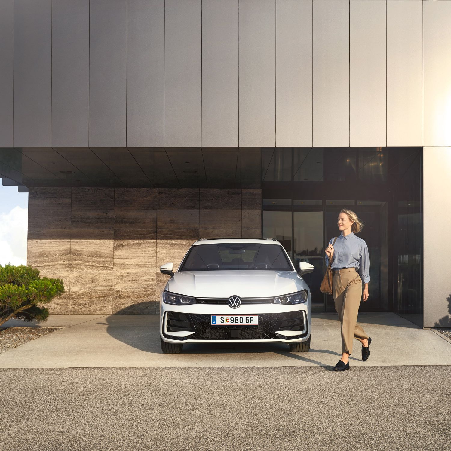 Frontansicht eines weißen VW Passat R-Line, eine Frau geht an ihm vorbei.