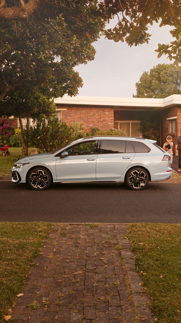 Ein weißer VW Golf Variant parkt vor einem Bungalow in einer Wohnstraße mit Bäumen. 