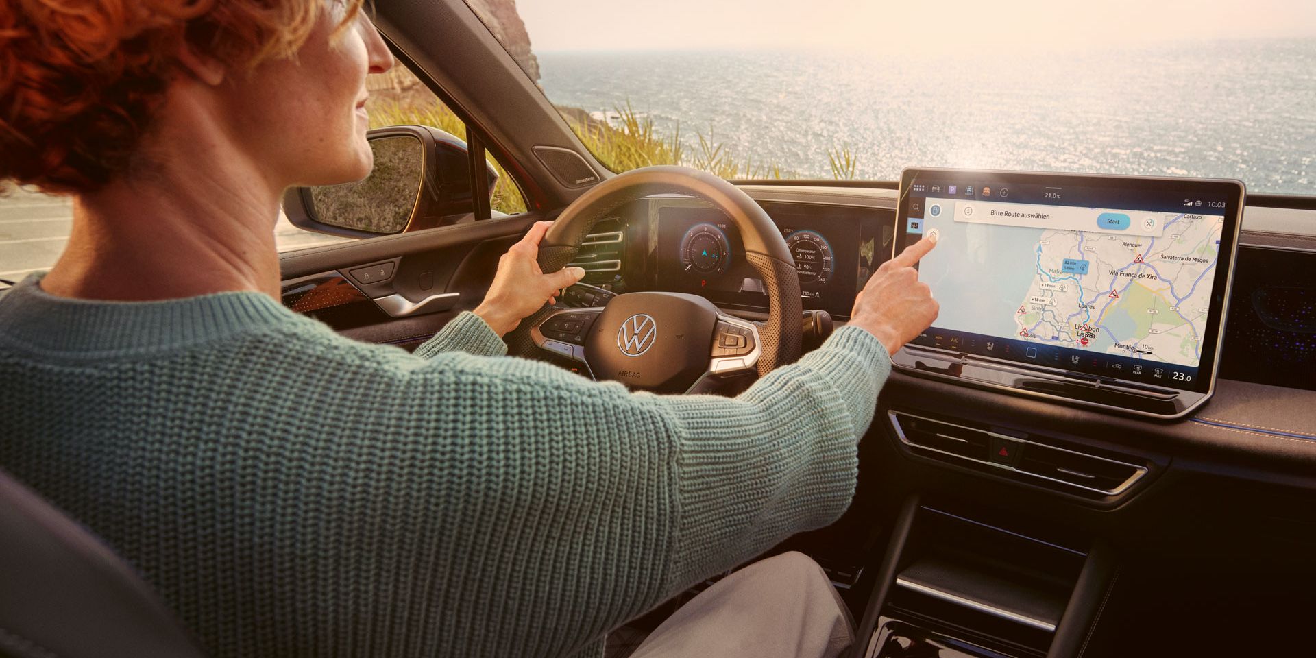 Frau sitzt auf dem Fahrersitz eines geparkten VW Tiguan und bedient den Touchscreen des Infotainment-Systems mit Kartenansicht.