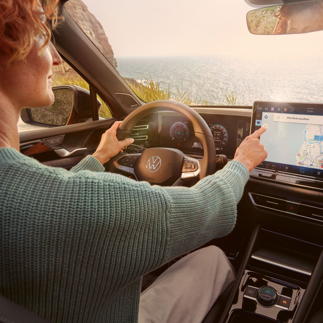 Frau sitzt auf dem Fahrersitz eines geparkten VW Tiguan und bedient den Touchscreen des Infotainment-Systems mit Kartenansicht.