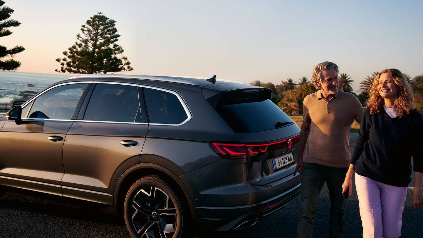 Ein Mann und eine Frau gehen an einem parkenden VW Touareg Elegance vorbei.