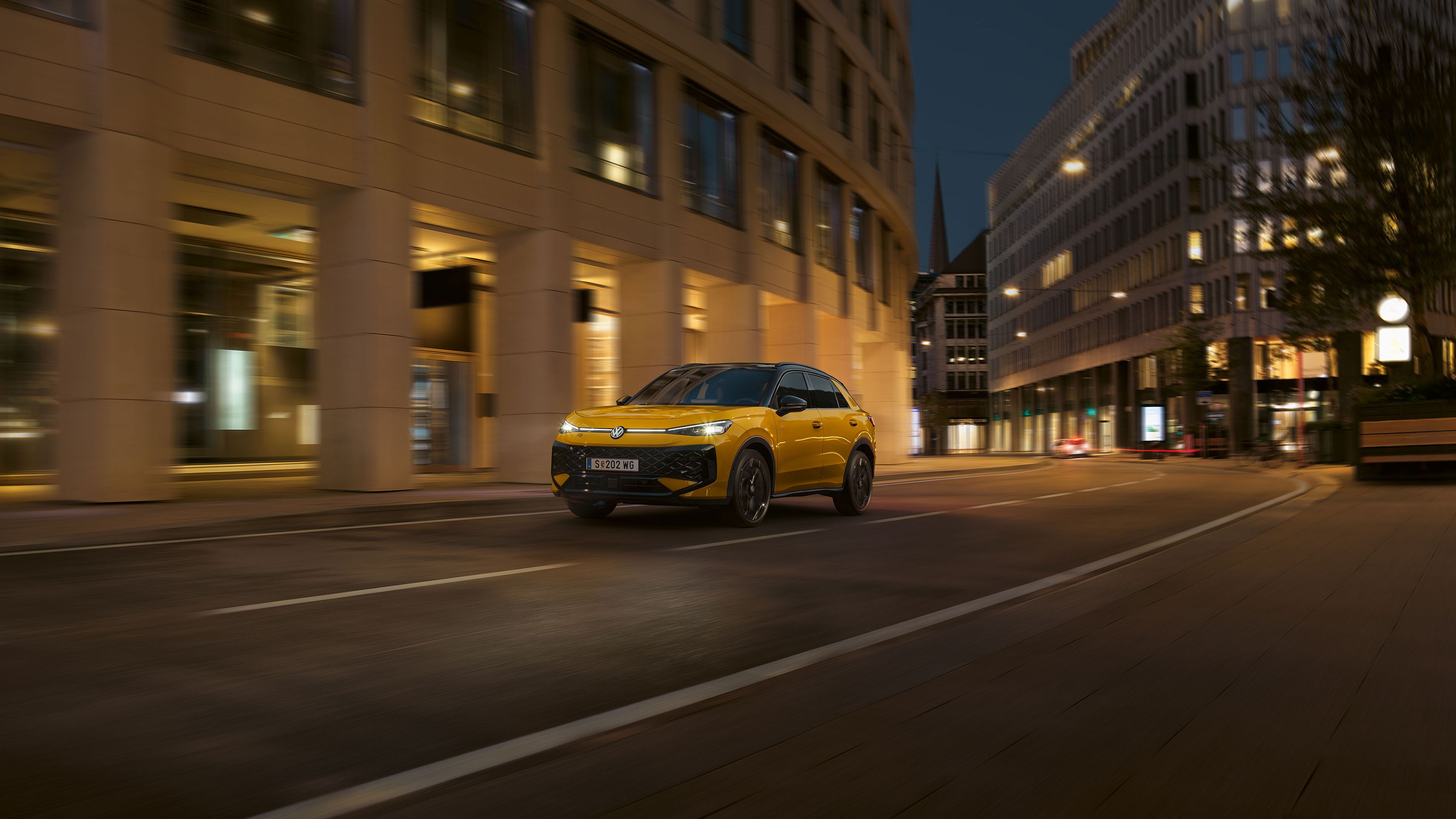Ein gelber VW T-Roc R-Line fährt nachts durch eine urbane Umgebung.