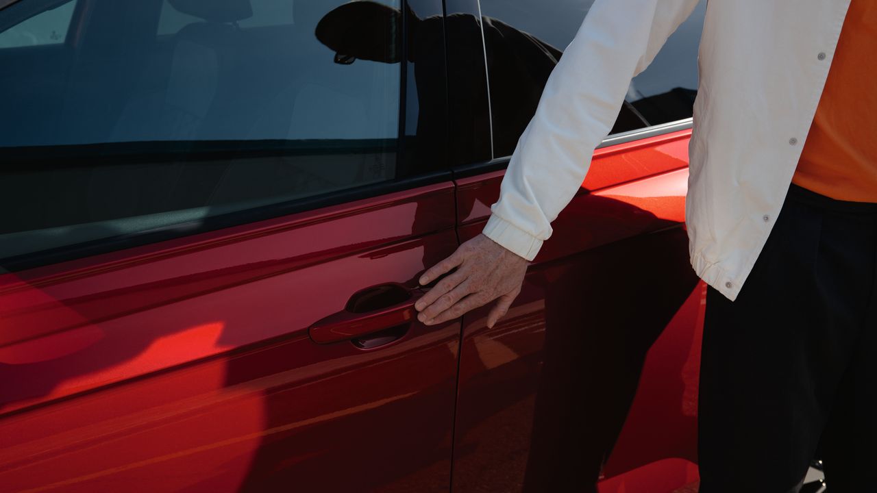 Detailansicht des Türgriffs eines roten VW Taigo, eine Hand berührt den Knopf für Keyless Access.