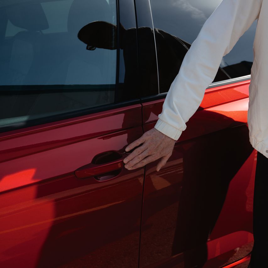 Detailansicht des Türgriffs eines roten VW Taigo, eine Hand berührt den Knopf für Keyless Access.