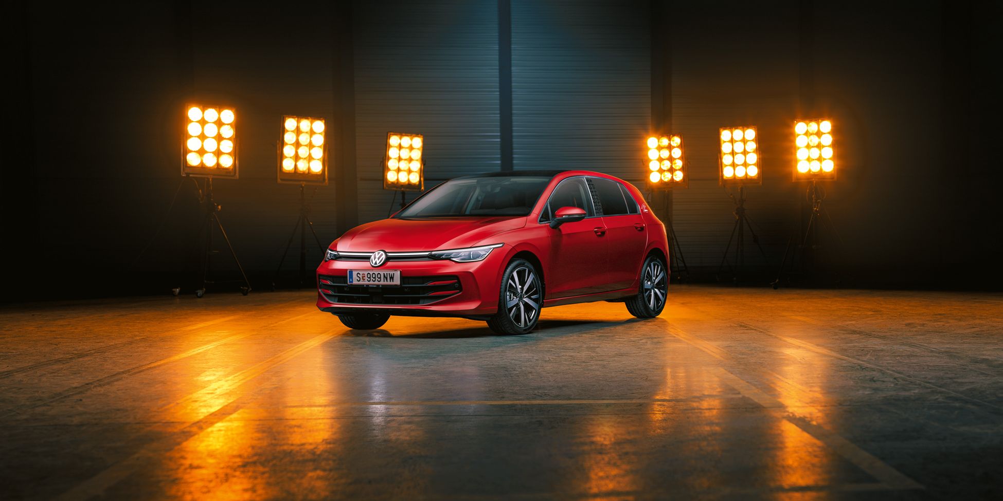 Ein roter Der VW Golf Falco Edition steht einer leeren Halle, dahinter Bühnenlicht.