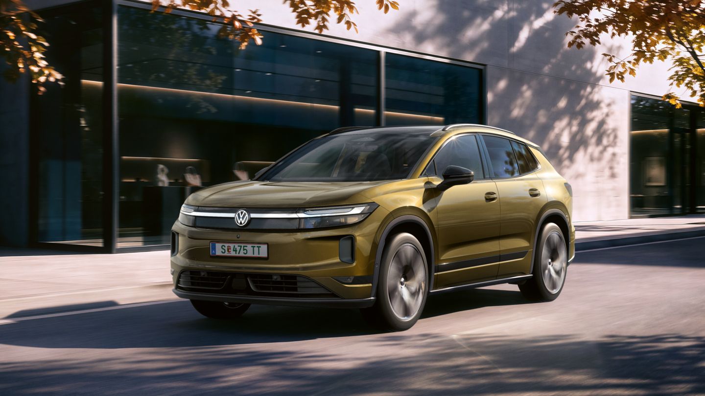 Ein oliv-bronzefarbener VW ID. Tiguan fährt auf einer Straße vor einem Bürogebäude.