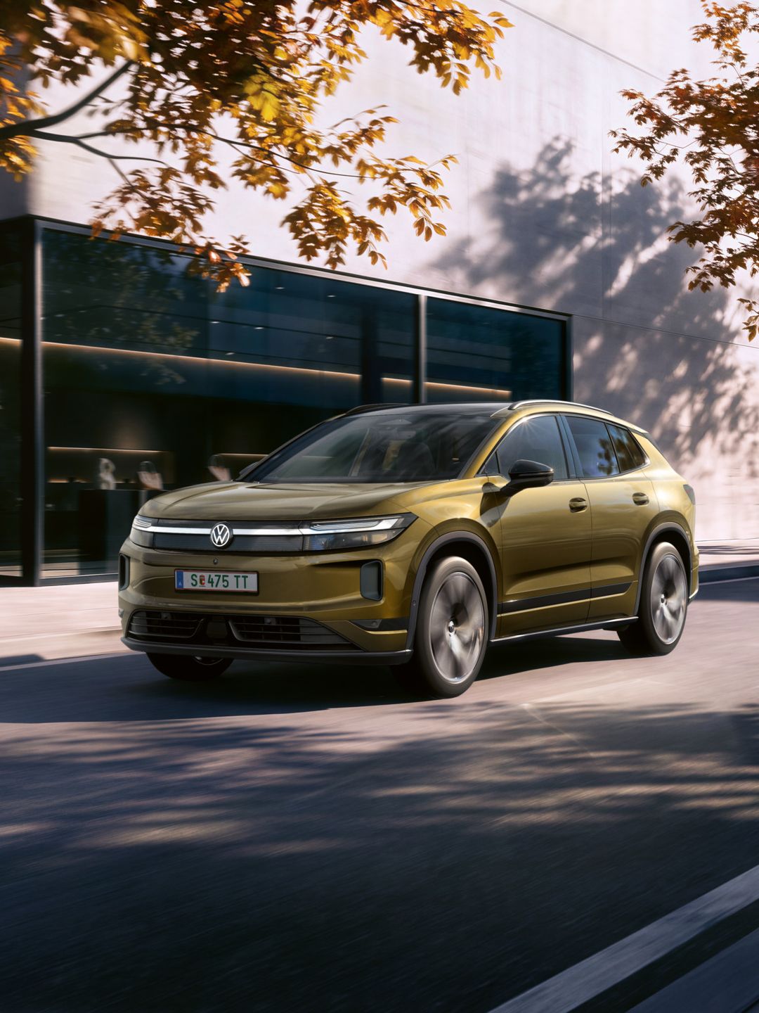 Ein oliv-bronzefarbener VW ID. Tiguan fährt auf einer Straße vor einem Bürogebäude.