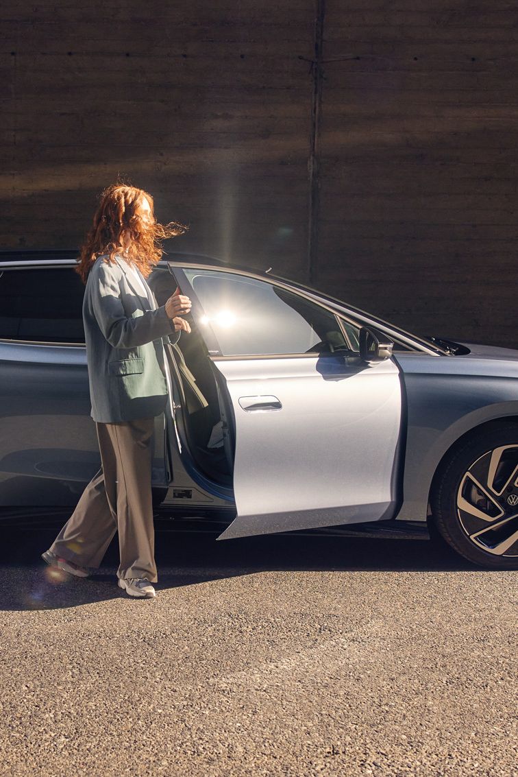 Eine Frau steht vor der geöffneten Beifahrertüre eines ID.7 Tourer 
