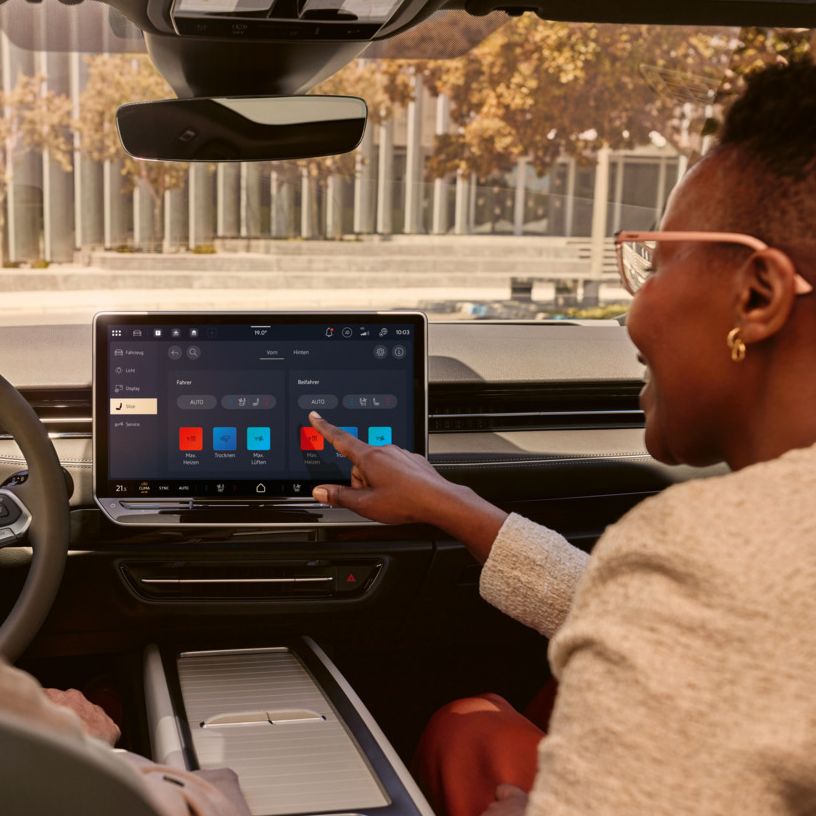 Zwei Frauen, die lachen, sitzen auf den Vordersitzen im VW ID.7 und bedienen das Infotainment-System.