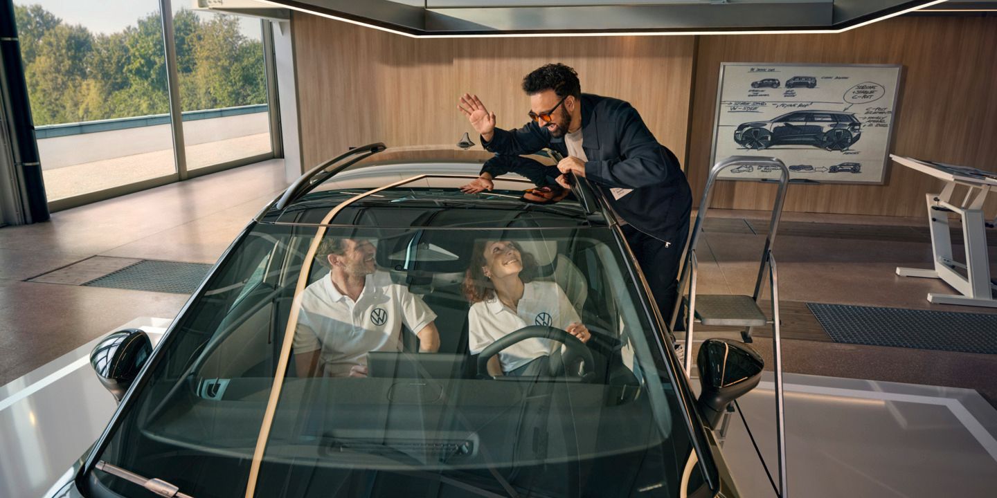 Ein Mann steht auf einer Leiter neben einem VW ID. Cross und winkt durch das Panoramadach den innen sitzenden Personen zu.
