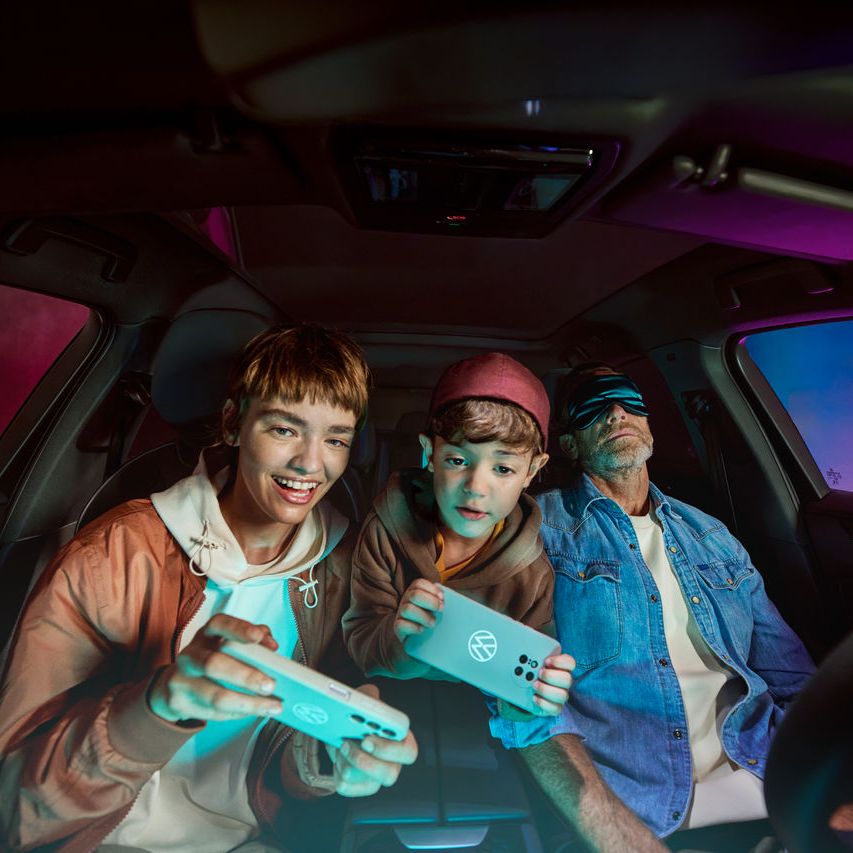 Vater mit zwei Kindern im Volkswagen, die Kinder spielen mit der AirConsole.