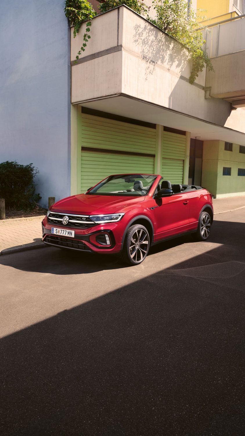 Roter T-Roc Cabriolet steht geparkt am Straßenrand neben dem Gehsteig in einer Stadt.