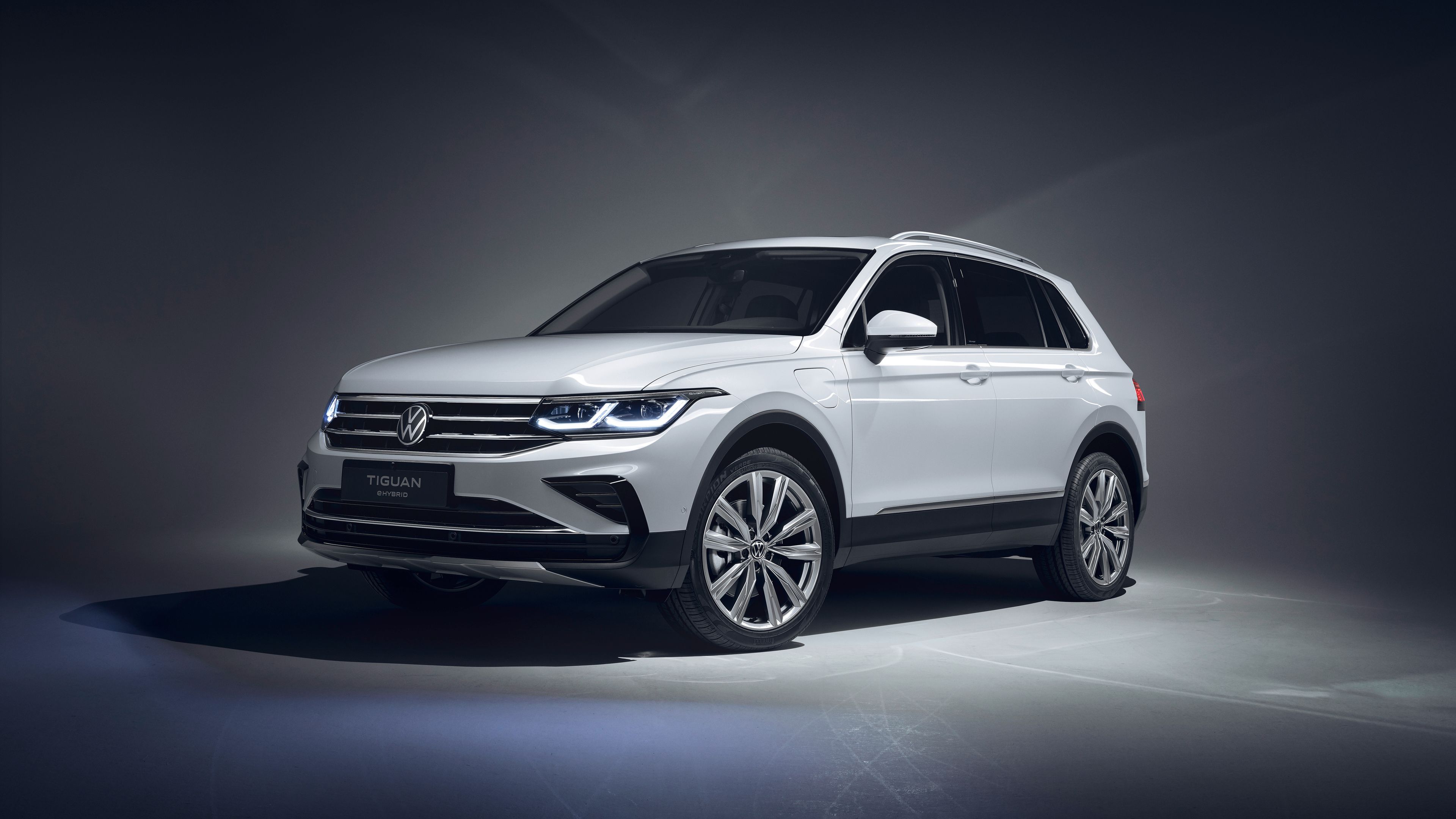 Ein silberner Volkswagen Tiguan steht in einem gut ausgeleuchteten Raum. Das Auto ist ein SUV-Modell und hat moderne, klare Linien. Es ist von vorne und der Seite sichtbar.