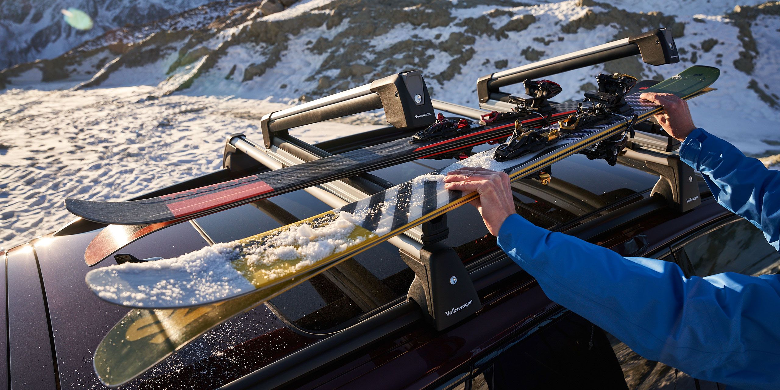 Am Skidachträger auf dem Dach eines Volkswagen werden zwei paar Ski befestigt.