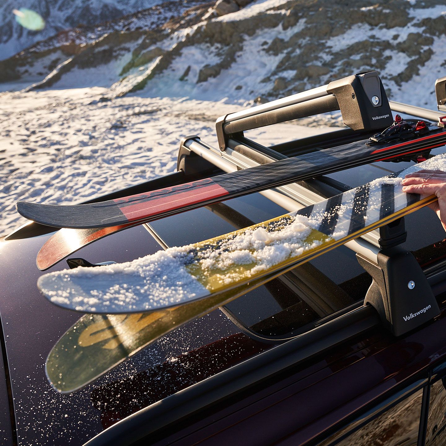 Am Skidachträger auf dem Dach eines Volkswagen werden zwei paar Ski befestigt.