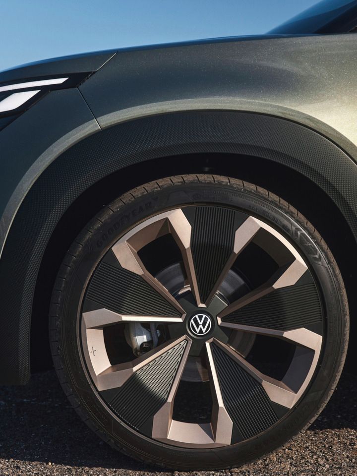 Nahaufnahme des vorderen rechten Radbereichs eines Volkswagen Elektroautos. Das Rad hat ein modernes, stylisches Design und der Hintergrund zeigt einen Wasserblick und einen klaren Himmel.