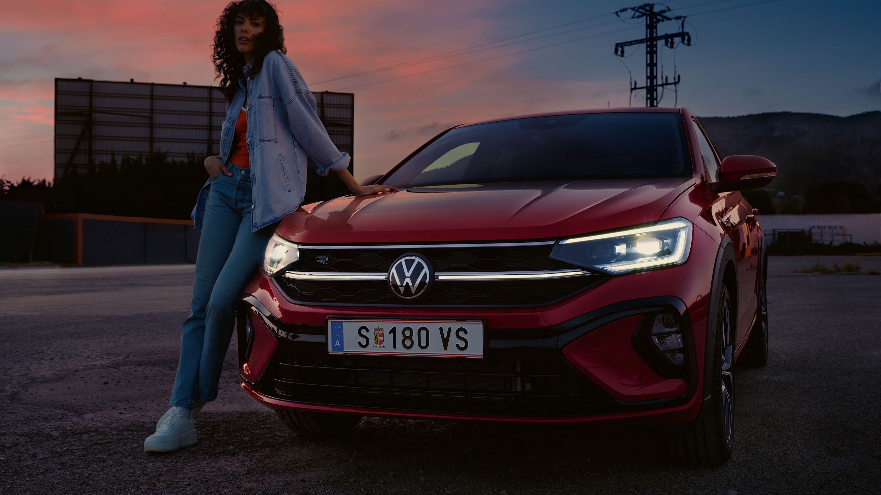 VW Taigo R-Line Front in Rot auf Parkplatz. Licht eingeschaltet. Frau lehnt an Motorhaube.